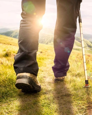 Person in Fruehpension am Wandern auf dem Gras in den Bergen.